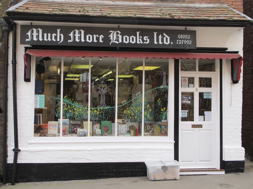 The shopfront of Much More Books at 6 High Street, Much Wenlock, with its black fascia, gold lettering and red awning